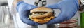 Scientist in rubber gloves hold hamburger in front of microscope and glass test tubes in chemical laboratory closeup