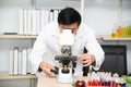 Scientist using Microscope in Laboratory. Male Researcher wearing white Coat sitting at Desk and looking at Samples.