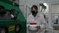 Scientist wearing protective suit and carrying a jar of toxic liquid inside a biohazard area