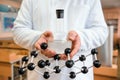 A scientist, in a white coat, holds a flask and a model of a molecule in his hands.