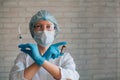 Scientist woman wearing protective suit and mask holds in crossed hands syringe and ampule. Female doctor in hospital ready for