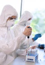 Scientists in protection suits and masks working in research lab using laboratory equipment: microscopes, test tubes.