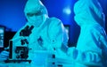 Scientists in protection suits and masks working in research lab using laboratory equipment: microscopes, test tubes