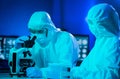 Scientists in protection suits and masks working in research lab using laboratory equipment: microscopes, test tubes