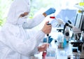 Scientists in protection suits and masks working in research lab using laboratory equipment: microscopes, test tubes.