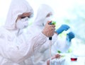 Scientists in protection suits and masks working in research lab using laboratory equipment: microscopes, test tubes.