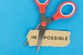 Scissor cutting the text `impossible` in a piece of paper
