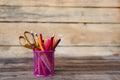 Scissors and colorful pencils of violet yellow pink red and orange in stationary cup on wooden table and background. Copyspace