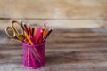 Scissors and colorful pencils of violet yellow pink red and orange in stationary cup on wooden table and background Royalty Free Stock Photo