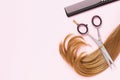 Scissors, a comb and a cut strand of light colored female childrens hair with copy space on a pink background Royalty Free Stock Photo