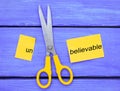 Scissors cut the word unbelievable. concept believable. cuts the Royalty Free Stock Photo