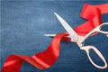 Scissors cutting red ribbon, close-up view on blue Royalty Free Stock Photo