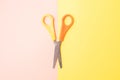 Scissors with yellow and orange handle on light pastel pink and yellow background Royalty Free Stock Photo