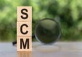 SCM Supply Chain Management abbreviation. Wooden cubes with letters, on a table with a magnifying glass. Green background.