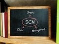 SCM Supply Chain Management inscription. Bookshelf with multicolor books and chalkboard