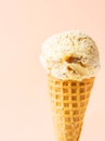 Scoop of delicious salted caramel toffee vanilla ice cream in waffle cone on pastel peachy pink background. Summer desserts