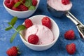 A scoop of homemade raspberry ice cream with fresh raspberries and mint in a white cup on a blue background. Delicious and Royalty Free Stock Photo