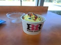 Scoop of Baskin Robbins Ice Cream in a Paper Cup with Colorful Sprinkles on Top, Transparent Plastic Cover on Table, Summer Treat