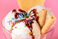 Scoops of ice cream in glass bowl with chocolate sauce, strewed sprinkles and cookies on pink background, close up Royalty Free Stock Photo