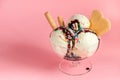 vanilla flavor ice cream in glass bowl with chocolate sauce, strewed sprinkles and waffle cookies on pink background