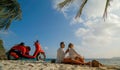 Scooter road trip. Lovely couple on red motorbike in white clothes on sand beach. People walking near the tropical palm Royalty Free Stock Photo