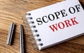 SCOPE OF WORK text on notebook with pen on wooden background