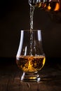 Scotch Whiskey without ice pouring out of the bottle, rustic wood background, copy space