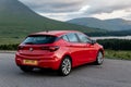 Red Vauxhall Astra hatchback parked in Scottish Highlands with a view at cloudy landscape when travelling across Scotland