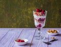 Scottish dessert Cranachan made of raspberries, oatmeal or granola and whipped cream in a glass goblet on a purple wooden