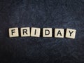 Scrabble letter tiles on black slate background spelling Friday