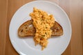 Scrambled egg served across a slice of buttered sourdough toast on a white plate Royalty Free Stock Photo