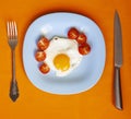 Scrambled eggs with cherry tomatoes on a blue plate, fork and knife on an orange background, top view Royalty Free Stock Photo