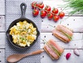 Scrambled eggs with chives in a cast iron pan, toasts with salmon and chives, and tomatoes. Healthy breakfasts on an old wooden wh