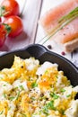 Scrambled eggs with chives in a cast iron pan, toasts with salmon and chives, and tomatoes. Healthy breakfasts on an old wooden wh