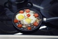 Scrambled eggs cooking in a frying pan, cooking on a ceramic stove, fried eggs with bacon and tomato, top view closeup Royalty Free Stock Photo