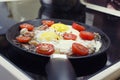 Scrambled eggs cooking in a frying pan, cooking on a ceramic stove, fried eggs with bacon and tomato, front view closeup Royalty Free Stock Photo