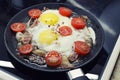 Scrambled eggs cooking in a frying pan, cooking on a ceramic stove, fried eggs with bacon and tomato Royalty Free Stock Photo