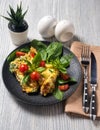 Scrambled eggs omelette portion for breakfast decorated with basil leaves and cherry tomatoes on a black porcelain plate. Knife Royalty Free Stock Photo