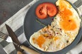 Scrambled eggs with thyme and pepper and spices, a piece of fresh tomato on a gray plate  a gray background, fork, knife Royalty Free Stock Photo