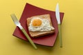 Scrambled eggs on toaster fried bread on quadrangular red plate and a fork with a knife on a yellow table Royalty Free Stock Photo