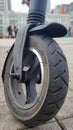 Scratched and damaged front wheel of an electric scooter on a city street against the background of paving slabs. Old e-scooter