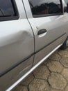 Scratched and dented side of a silver gray car right next to the door handle, with wall paint marks in need of a body shop and