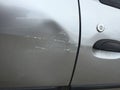 Scratched and dented side of a silver gray car right next to the door handle, with wall paint marks. Royalty Free Stock Photo