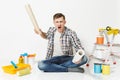 Screaming aggressive angry young man with rolls of wallpaper, sitting on floor with instruments for renovation apartment