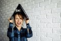 Screaming female freelancer with laptop on head while standing nearwhite brick wall.