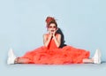 Screaming girl with colorful dreadlocks in bright coral big dress, sneakers, sunglasses sitting on floor legs wide apart Royalty Free Stock Photo