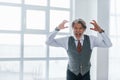 Screaming senior man in jacket and tie indoors in room against window Royalty Free Stock Photo