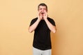 Screaming traumatized man in black T-shirt with bruises and abrasions on his face isolated over beige background shouting loud