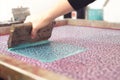 A screen printing squeegee is guided by hand over a silk-screen and shoves cyan paint over a detailed clover design