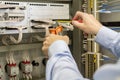 Screwdriver and wire cutters in hands of electrician against electric box with terminal, wires and controllers